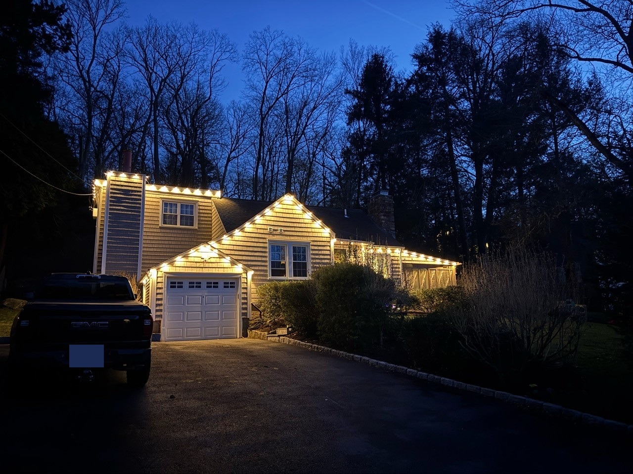 Driveway view of the same home with warm white lights outlining its roof and garage