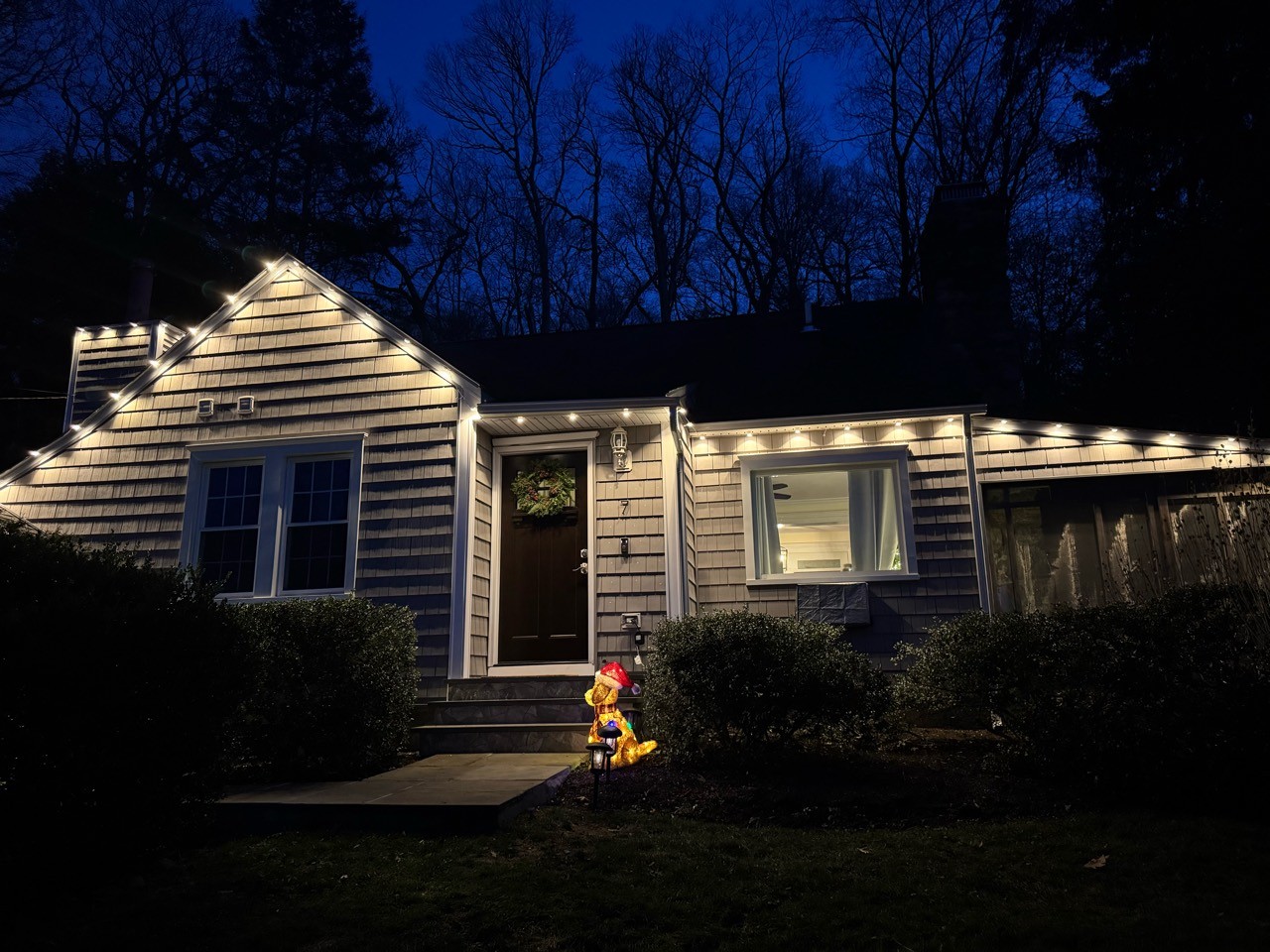 Warm white Christmas lights outlining the front roofline and entry of a real installation at dusk